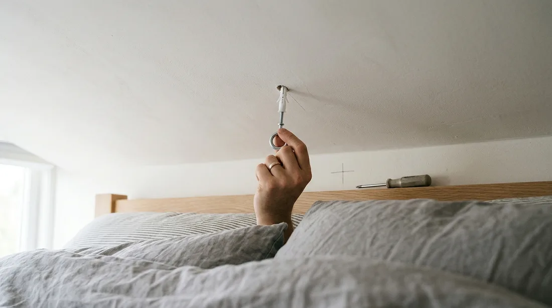 Deckenhaken mit Dübel wird über einem Bett in die Zimmerdecke gesetzt